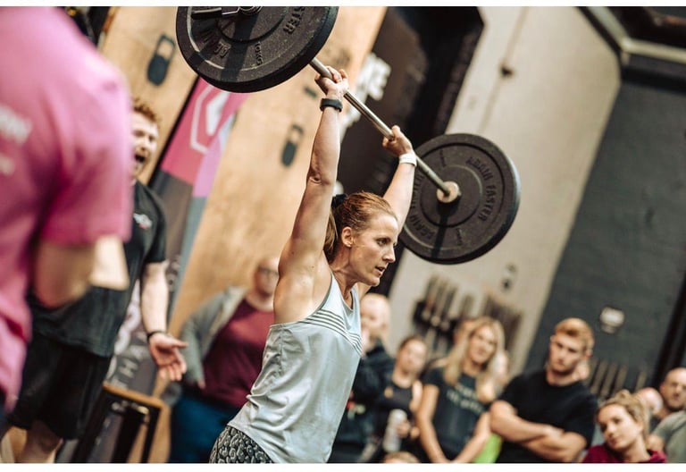Athlete performing an overhead barbell lift in a gym with spectators watching in the background
