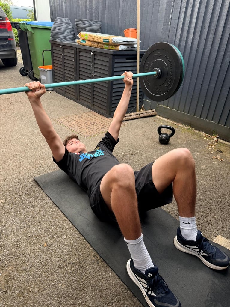 Man performing a barbell exercise on a mat outdoors, lifting a turquoise barbell with weights overhead