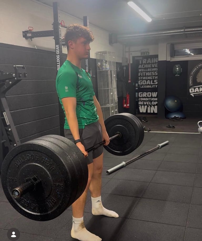 Man in green shirt performing weightlifting exercise with barbell in a gym with motivational wall signage
