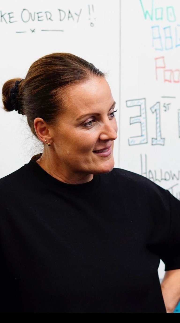 Woman in black shirt smiling in profile with whiteboard covered in handwritten text in background