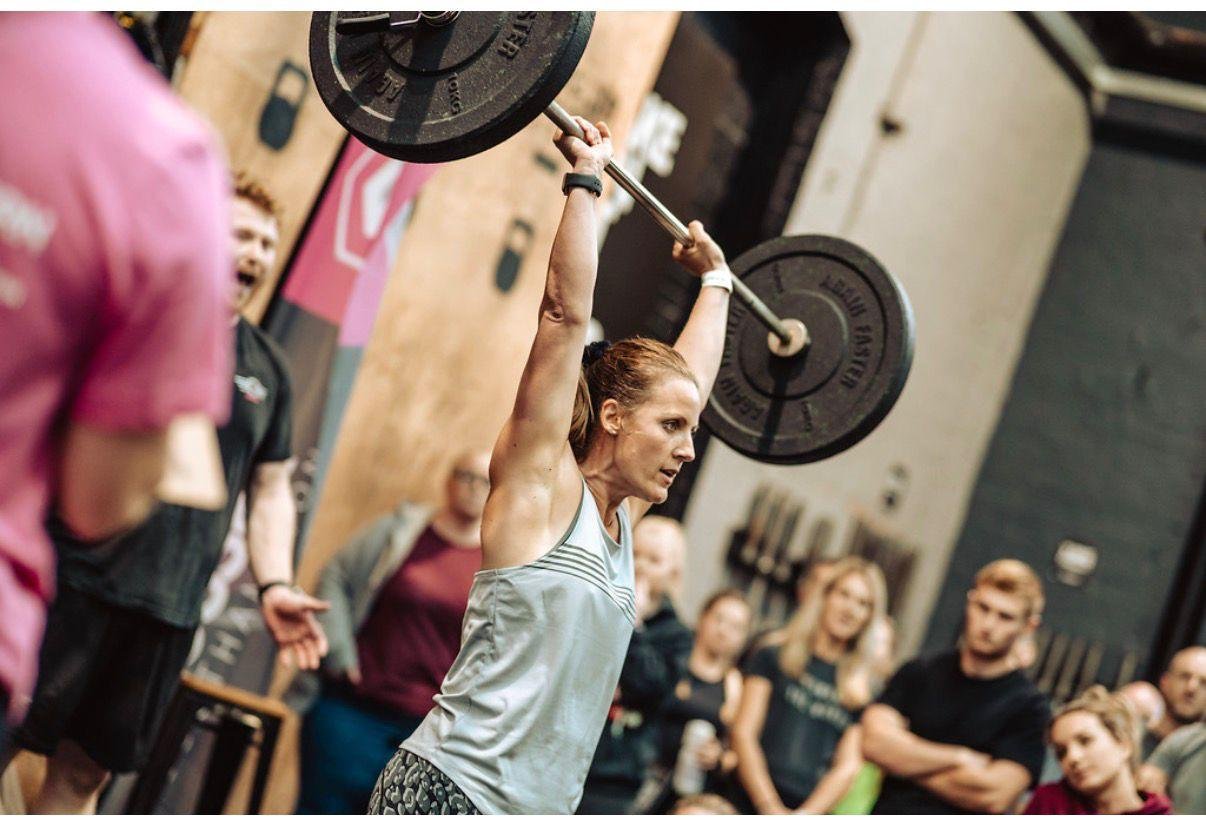 Athlete lifting barbell overhead in crossfit gym with spectators watching