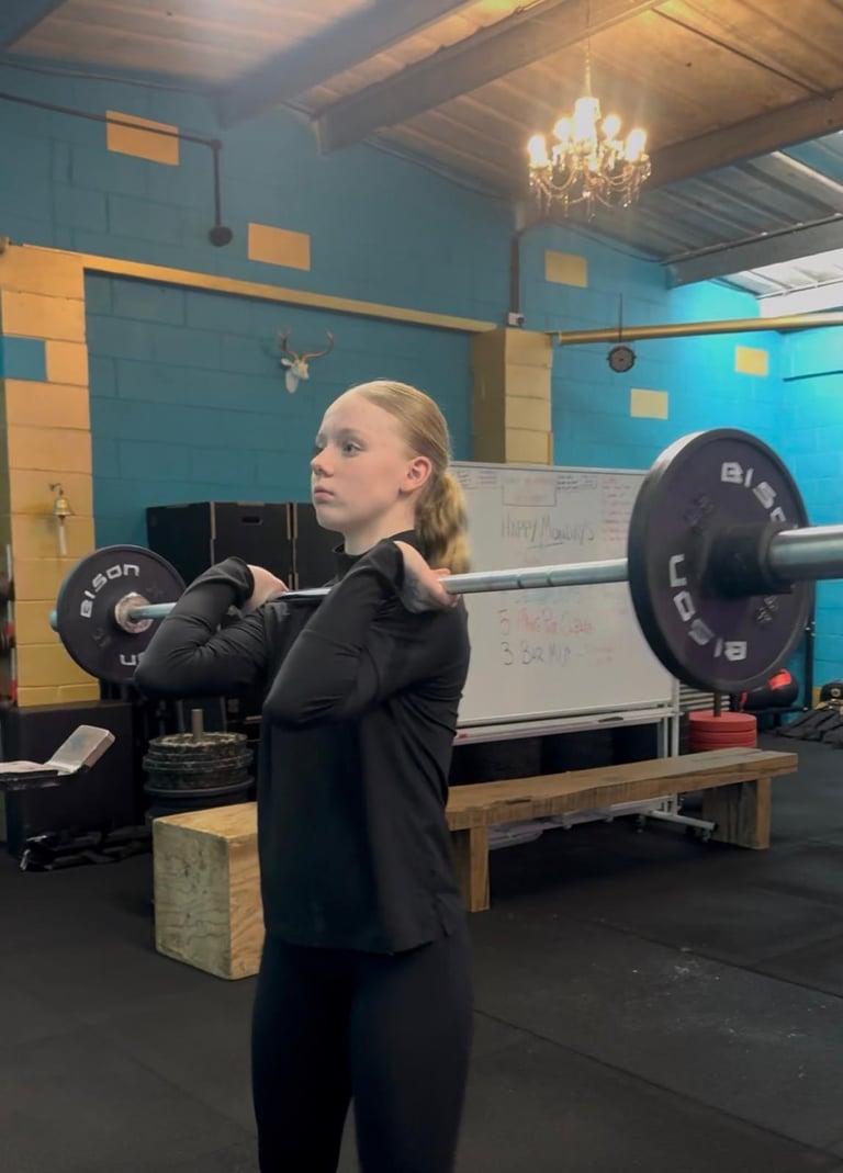 Young woman performing barbell deadlift in crossfit gym with blue walls and chandelier